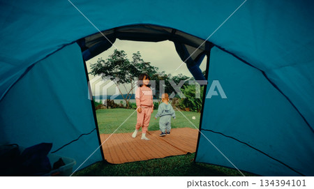 Children play outside a colorful tent in a scenic campground on a summer day Children play outside a colorful tent in a scenic campground on a summer day 134394101