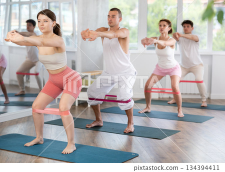 Young men and women practicing half squat with band standing on mat 134394411