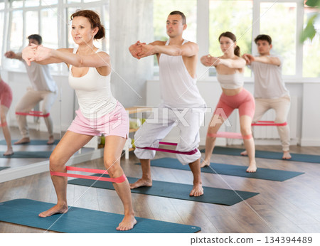 Young men and women practicing half squat with band standing on mat 134394489