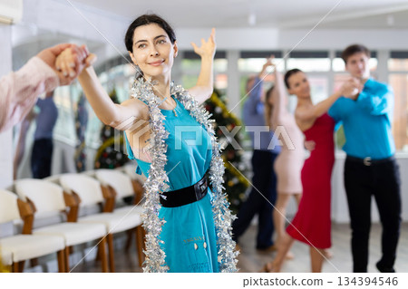 Young brunette in blue dress dancing salsa with partner during Christmas party 134394546