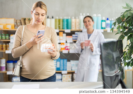 Pregnant woman scan QR code on vitamin pills product, pharmacist offer similar product in background 134394549