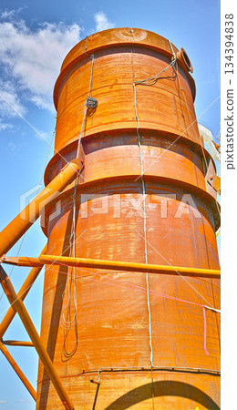 A tall silo water tower against a blue sky background from below. An orange storage tank for the farming or agriculture industry used for large scale grain or wheat production on a farm A tall silo water tower against a blue sky background from below. An orange storage tank for the farming or agriculture industry used for large scale grain or wheat production on a farm 134394838