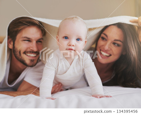 Mother, father and baby under blanket on bed for love, care and quality time together. Portrait of playful child, happy family and kids relaxing in bedroom with bedding fort, fun and bonding in house Mother, father and baby under blanket on bed for love, care and quality time together. Portrait of playful child, happy family and kids relaxing in bedroom with bedding fort, fun and bonding in house 134395456