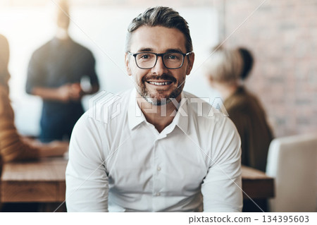 Leadership, portrait of ceo or businessman smile and sitting in office at work with colleagues behind manager. Entrepreneur or business, leader and smiling male person with glasses sit at workplace Leadership, portrait of ceo or businessman smile and sitting in office at work with colleagues behind manager. Entrepreneur or business, leader and smiling male person with glasses sit at workplace 134395603