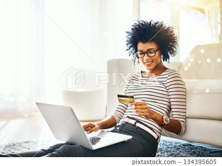 Young woman, laptop and credit card with bokeh doing online shopping sitting on ground. Home, happiness and computer of happy African female person on a web ecommerce app reading an internet deal Young woman, laptop and credit card with bokeh doing online shopping sitting on ground. Home, happiness and computer of happy African female person on a web ecommerce app reading an internet deal 134395605