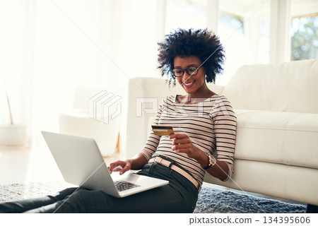 Young woman, laptop and credit card on living room rug doing online shopping sitting on ground. Home, happiness and computer with African female person on a ecommerce app reading information to buy 134395606