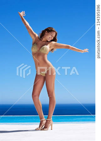 Freedom, travel and woman in bikini by a swimming pool while on summer vacation, holiday or adventure. Blue sky, fashion and body of female model posing in swimwear by water on tropical weekend trip. Freedom, travel and woman in bikini by a swimming pool while on summer vacation, holiday or adventure. Blue sky, fashion and body of female model posing in swimwear by water on tropical weekend trip. 134395896