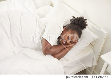 Peaceful smiling African American woman sleeping comfortably in bed, enjoying sunny weekend morning. 134396344