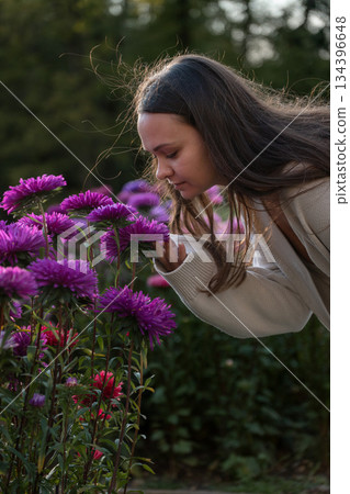 Young woman smells purple flowers in a garden, side view portrait, soft daylight, rich green and violet tones, gentle and mindful mood 134396648