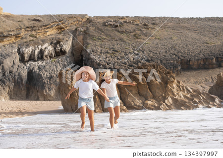 Happy girls running in sea water on beach during Happy girls running in sea water on beach during 134397997