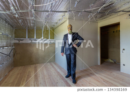 Strange man in businessman suit and gas protection mask inside a room under renovation works. Strange man in businessman suit and gas protection mask inside a room under renovation works. 134398169