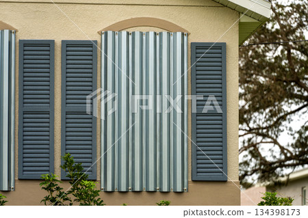 Storm resistant steel shutters cover windows of Florida house as precaution before hurricane. Home prepared for extreme weather Storm resistant steel shutters cover windows of Florida house as precaution before hurricane. Home prepared for extreme weather 134398173