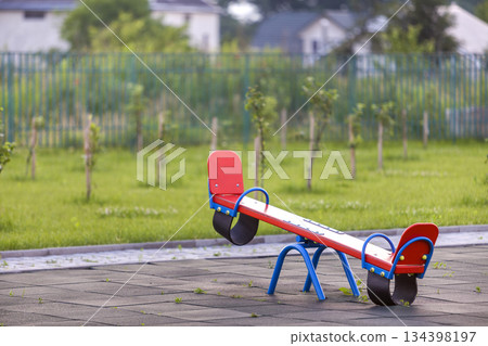 Seesaw swing in big yard with soft rubber flooring on sunny summer day. 134398197