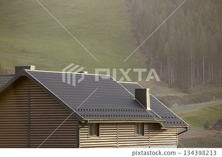 Roof of cottage with siding walls, brown shingle roof and high chimneys in ecological area on foggy landscape copy space background on sunny summer day. Well maintained property, real estate concept. Roof of cottage with siding walls, brown shingle roof and high chimneys in ecological area on foggy landscape copy space background on sunny summer day. Well maintained property, real estate concept. 134398213