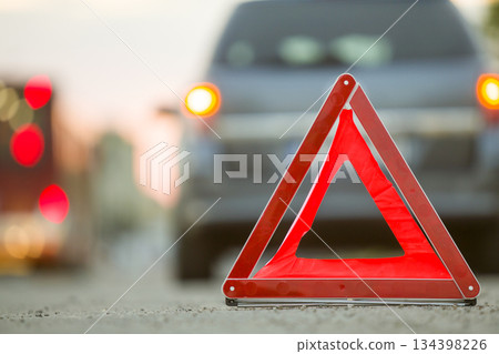 Red emergency triangle stop sign and broken car on a city street. Red emergency triangle stop sign and broken car on a city street. 134398226