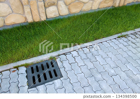 Plastic drain gutter, green grass lawn and stone pavement sidewalk. Plastic drain gutter, green grass lawn and stone pavement sidewalk. 134398500