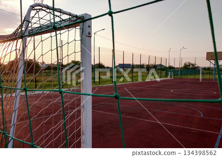 Outdoors mini football and basketball court with ball gate and basket surrounded with high protective fence. 134398562