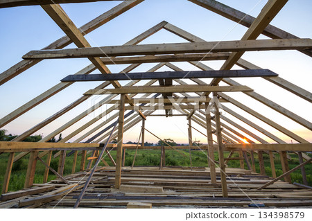 New wooden house under construction. Close-up of attic roof frame against clear sky from inside. Ecological dream home of natural materials. Building, construction and renovation concept. New wooden house under construction. Close-up of attic roof frame against clear sky from inside. Ecological dream home of natural materials. Building, construction and renovation concept. 134398579