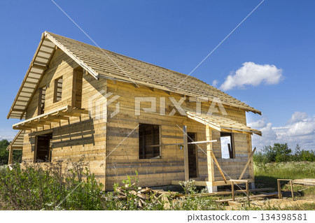 New wooden ecological traditional cottage of natural lumber materials with steep roof under construction in green neighborhood on blue sky copy space background. Professional building concept. 134398581