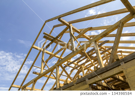New wooden ecological house from natural materials under construction. Close-up detail of attic roof frame against clear sky. Building, roofing, construction and renovation concept. 134398584