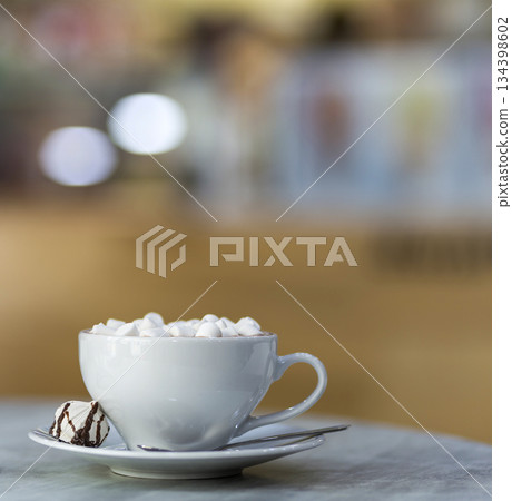 Mug of coffee with marshmallows on porcelain plate on blurred colorful interior bokeh background. 134398602