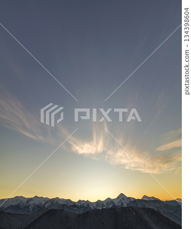 Mountain winter panorama landscape at dawn. Steep mountain peaks covered with snow and woody hills with spruce forest, raising bright sun on clear blue sky at sunrise copy space background. 134398604