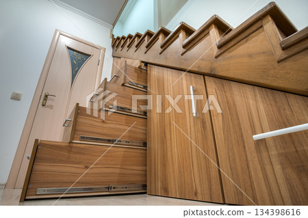 Modern architecture interior with luxury hallway with glossy wooden stairs in multi-storey house. Custom built pullout cabinets on glides in slots under stairs. Use of space for storage. 134398616