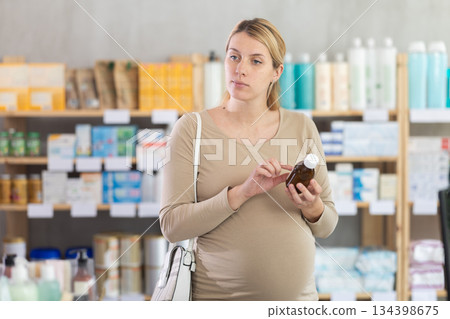 Pregnant woman customer choosing syrup in drugstore Pregnant woman customer choosing syrup in drugstore 134398675