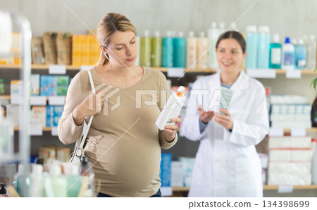 Pregnant woman choose diaper rash cream in pharmacy, pharmacist in background offer similar product Pregnant woman choose diaper rash cream in pharmacy, pharmacist in background offer similar product 134398699