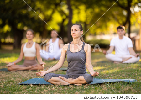 Yoga lesson visitors with girl coach perform padmasana in park Yoga lesson visitors with girl coach perform padmasana in park 134398715