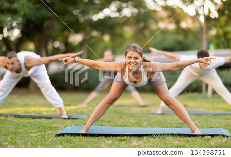 Yoga lesson visitors with coach perform Prasarita Padottanasana in park Yoga lesson visitors with coach perform Prasarita Padottanasana in park 134398751
