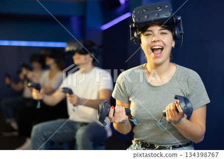 Excited young girl with VR glasses and controllers in virtual reality room Excited young girl with VR glasses and controllers in virtual reality room 134398767
