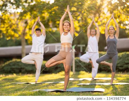 Girl doing Vrikshasana asana at group yoga session in park 134398774
