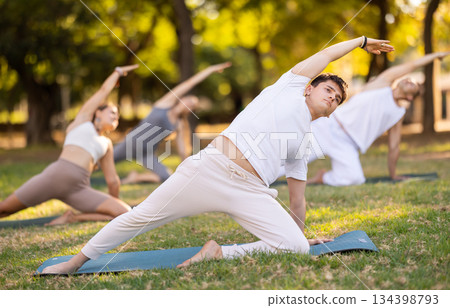 Guy doing Reverse Gate Pose during group yoga in park Guy doing Reverse Gate Pose during group yoga in park 134398793