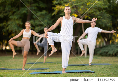 Yoga lesson visitors with coach perform Parivritta Hasta Padangushthasana in park Yoga lesson visitors with coach perform Parivritta Hasta Padangushthasana in park 134398799