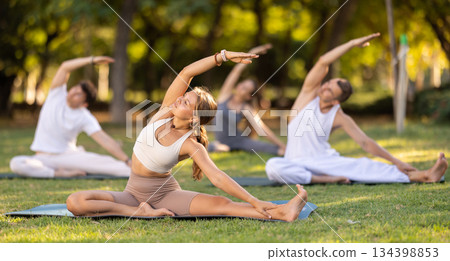 Girl participating in outdoor group yoga session in summer park 134398853