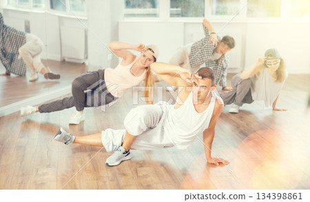 Man and his students perform hip hop dance on one bent leg, movement in horizontal plane near floor 134398861