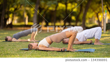 Girl performing Setu Bandha Sarvangasana during group yoga in park 134398891