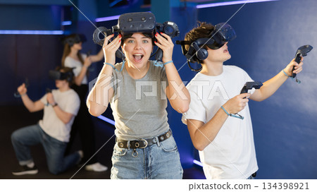 Excited young girl with VR glasses and controllers in virtual reality room 134398921