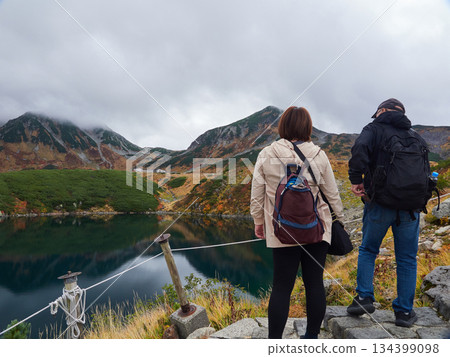 Autumn tourist attraction Tateyama Kurobe Alpine Route: Senior male and female tourists resting at Mikurigaike Pond on the summit of Murodo Mountain and mountain scenery Autumn tourist attraction Tateyama Kurobe Alpine Route: Senior male and female tourists resting at Mikurigaike Pond on the summit of Murodo Mountain and mountain scenery 134399098