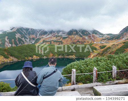 秋季旅遊景點館山黑部阿爾卑斯山脈路線:老年男女遊客在室堂山頂的御栗池畔休息,欣賞山景。 秋季旅遊景點館山黑部阿爾卑斯山脈路線:老年男女遊客在室堂山頂的御栗池畔休息,欣賞山景。 134399271