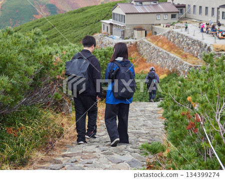 Autumn tourist attraction: Young couple tourists walking at the top of Mt. Murodo on the Tateyama Kurobe Alpine Route and mountain scenery Autumn tourist attraction: Young couple tourists walking at the top of Mt. Murodo on the Tateyama Kurobe Alpine Route and mountain scenery 134399274