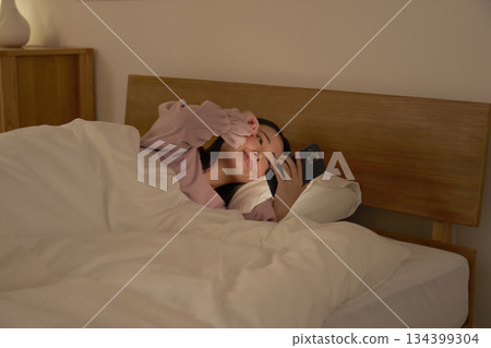 一位女士在床上使用智慧型手機，感覺很睏 134399304