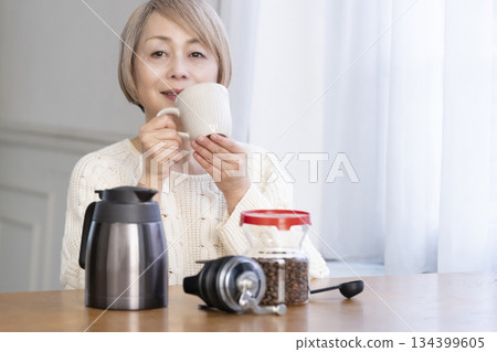 A senior woman relaxing in the living room, grinding coffee beans and drinking coffee 134399605