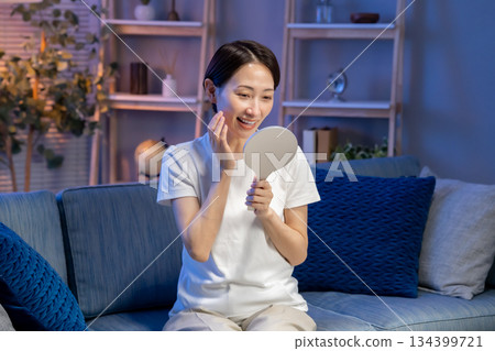 A woman looking at a hand mirror, smiling 134399721
