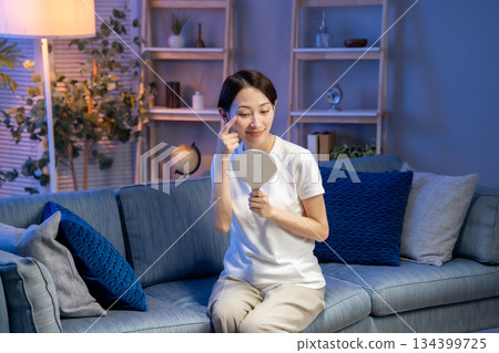 A woman looking at a hand mirror, smiling 134399725