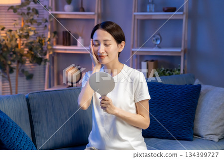 A woman looking at a hand mirror, smiling 134399727