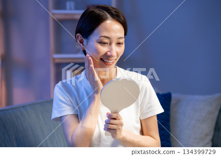 A woman looking at a hand mirror, smiling 134399729