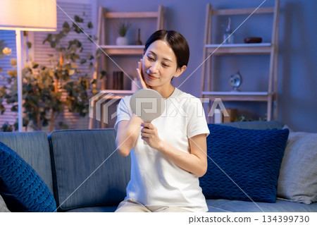 A woman looking at a hand mirror, smiling A woman looking at a hand mirror, smiling 134399730