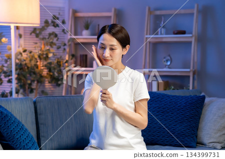 A woman looking at a hand mirror, smiling 134399731